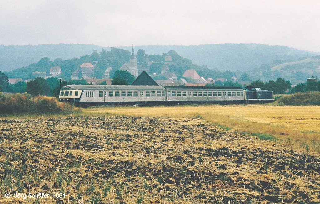 Eine 1991 typische Wendezuugarnitur vor Burgbernheim mit seinem Hausberg. Auf der im Hintergrund sichtbaren Frankenhhe liegt der Haltepunkt  Burgbernheim Wildbad  der Hauptstrecke Wrzburg-Ansbach.
