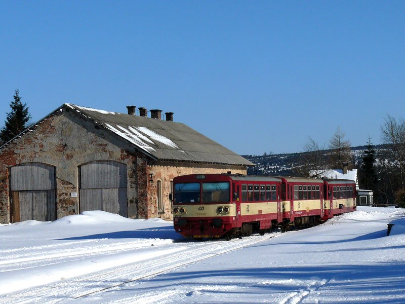 Eine Sandwich-Garnitur bestehend aus zwei 810er Triebwagen und einem Beiwagen passiert bei Ausfahrt aus Moldava (Moldau) den ehemaligen Lokschuppen; 07.03.2010