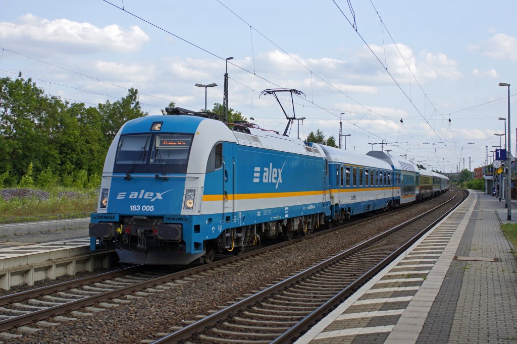 Einen recht bunt zusammengestellten Alex führt 183 005 ohne Halt durch den Bahnhof Neufahrn in Niederbayern. Neben den üblichen Alex-Wagen ist ein älterer DoSto-Wagen der Bauart Görlitz und weiter hinten ein Reisezugwagen im TEE-Farbschema eingereit. Auf dem Bild nicht zu sehen ist, dass auch Wagen in alter IC- (verkehrsrotes Fensterband) und IR-Farbgebung (fernblau) mitlaufen. 12.07.2013