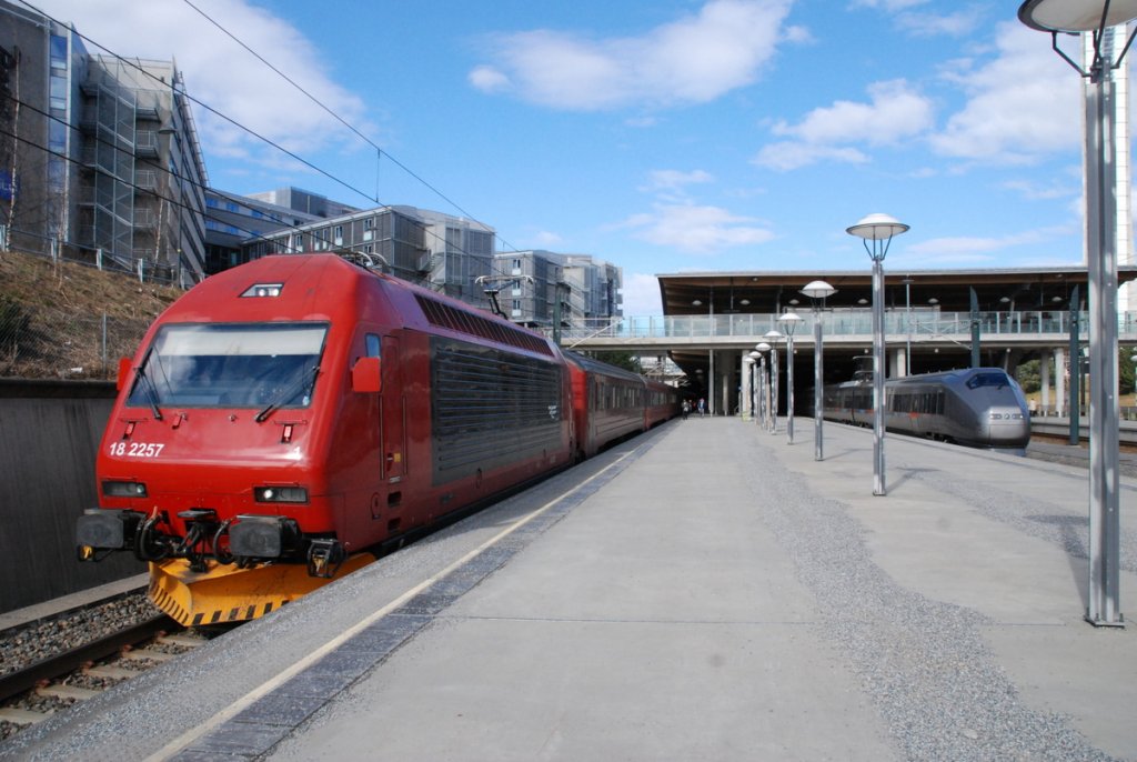 Flughafen Oslo Gardemoen: Am 13.04.2012 trifft ein Lokzug mit Lokomotive aus der Baureihe 18 - hier 18 2257 (SLM Winterthur - ADtranz) mit Personenzug bestehend aus lteren Personenwagen in unterschiedlicher Farbgebung - einen Flytoget aus dem Baumuster 71 - ebenfalls mit Ziel Oslo.