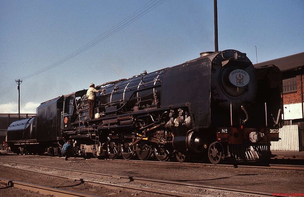 Für die Beförderung des  Drakensberg  wird die 25NC 3523 im Depot De Aar auf Hochglanz gebracht (generell präsentierten sich die meisten Dampflokomotiven zu diesem Zeitpunkt in einem äußerlich sehr guten Zustand). Dieser Zug bestand aus der alten, jetzt grün lackierten Wagengarnitur des Blue Train und verband Kapstadt mit  Durban. Im November 1976 war die Strecke De Aar - Kimberley das letzte Teilstück, auf dem dieser Zug noch von einer Dampflokomotive gezogen wurde.