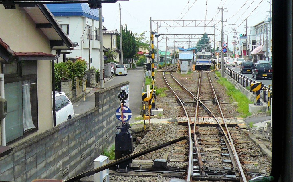Fukushima Verkehrsbetriebe: Auf einem grossen Teil der Strecke verluft die Bahn eingepfercht zwischen der Strasse und den kleinen Husern. Hier Einfahrt in die Kreuzungsstation Sasaya, wo Wagen 7206 bereits wartet. 11.Juli 2010. 