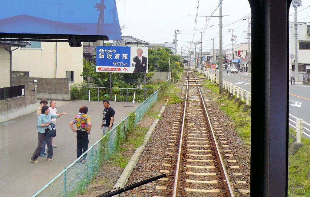 Fukushima Verkehrsbetriebe: Typischer Streckenabschnitt entlang der Strasse. Ganz offensichtlich luft hier ein grosser Streit ab! Und im Hintergrund wirbt ein grosses Plakat fr den Friedhof von Iizuka. Bild durch die verglaste Fhrerstandtre des Wagens 7101. Zwischen Iji-mae und Hirano, 11.Juli 2010.