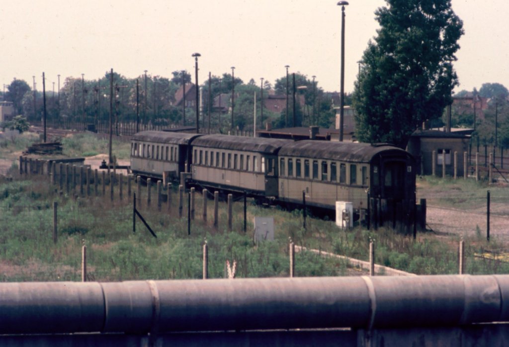 Grenzbahnhof Staaken (heute wieder Berlin)1975. Drei alte Wagen, die zuletzt als Baracken f�r die Angeh�rigen der Grenztruppen dienten. Diese Wagen waren durch einen Zaun vom Hinterland abgegrenzt, obwohl man dieses Gebiet nur mit Sonderausweis betreten konnte. Zwischen den Wagen und dem Grenzbahnhof noch ein Trennzaun. Hinten Links ein Wachturm, vorn die Mauerkrone und dahinter noch zwei Grenzz�une - was f�r ein Aufwand ...  Heute zum Gl�ck Alles weg.