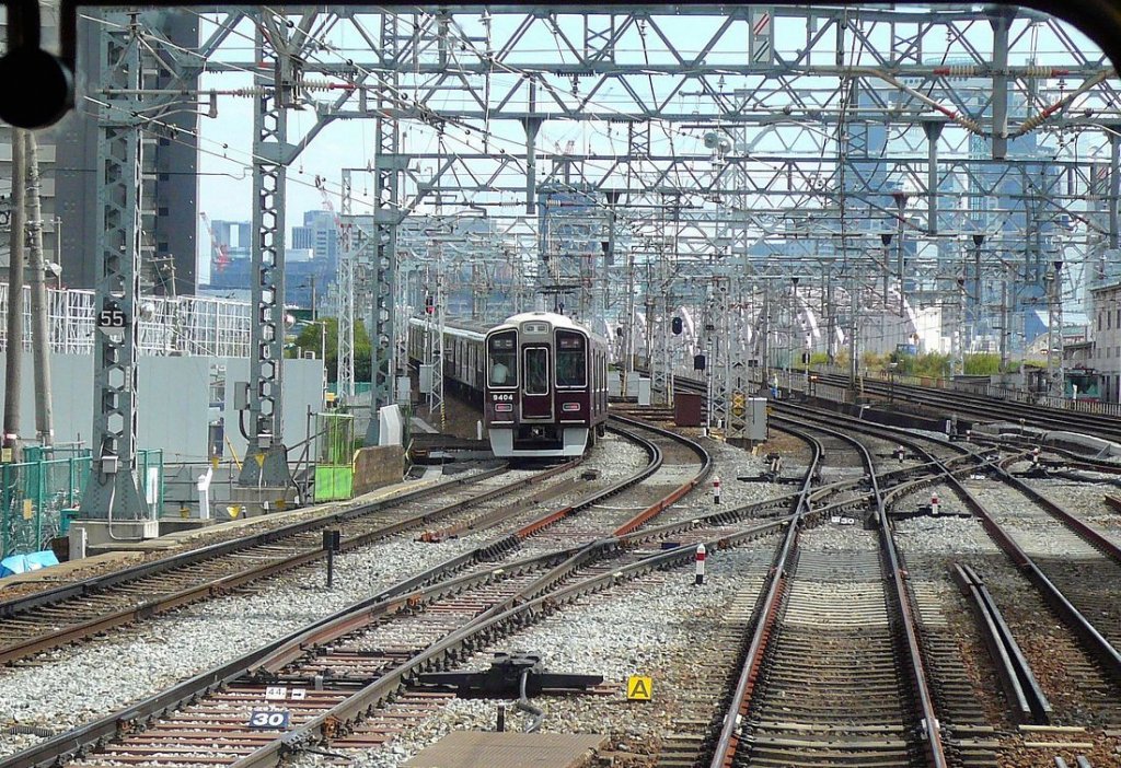 Grunddaten des Hankyû-Konzerns (Hankyû = Schnelle Verbindungen im Raum Osaka ): Riesiger Konzern, der täglich ca.2 Millionen Menschen befördert; 1435mm-Spur;146,6km Länge; 1907 eröffnet. Weltberühmt als Betreiber des Takarazuka Frauentheaters ( Takarazuka Revue ) oder auch für das erste Bahnhofswarenhaus (1929, in Osaka-Umeda), in dem man sich nach Ankunft bzw. vor der Heimfahrt mit allem eindecken konnte, was man brauchte. Seit 2005 in Sparten aufgeteilt: Eisenbahn/Immobilien/Freizeit/Handelsunternehmen + Hotelkette und Reisebüro. Enorme Schäden an den Strecken im Raum Osaka/Kobe beim schweren Erdbeben 1995. Im Bild überquert der ganz neue Zug 9304 (Endwagen 9404) den Fluss vor Erreichen des Hankyû-Hauptbahnhofs Osaka-Umeda, 28.September 2009.  Serie 9300: 2003-2010 erbaut. 