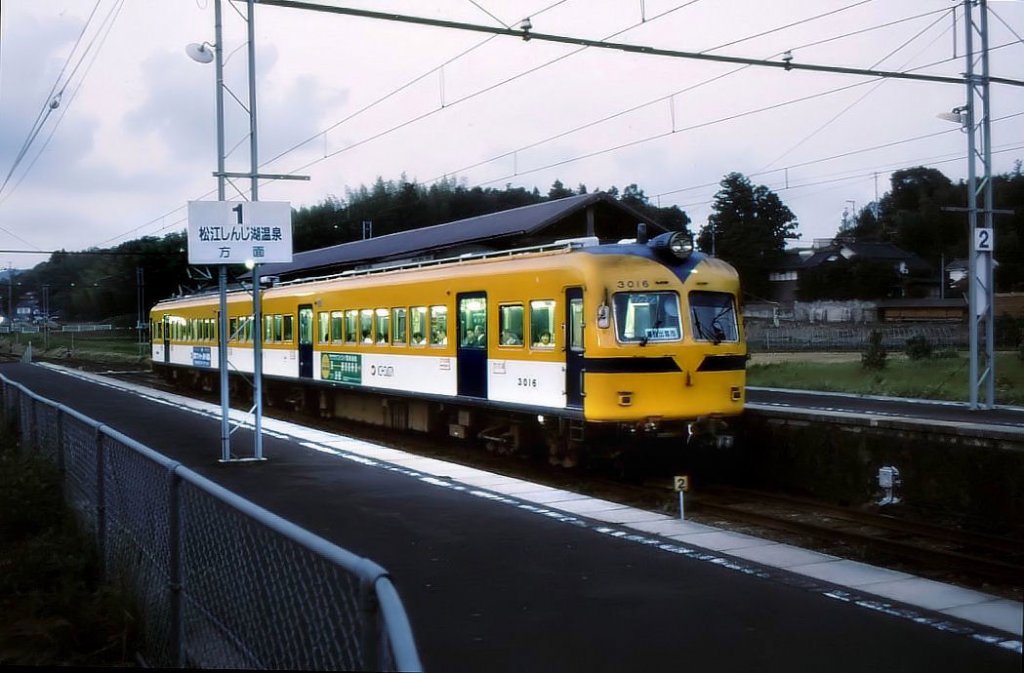 Grundstruktur des japanischen Eisenbahnnetzes (3): Im ganzen Land finden sich - meist elektrische - Privatbahnen, die vielfach recht armselig wirken. Ihre Fahrzeuge sind in der Regel gebraucht bernommene, alte Wagen. Hier steht ein Zug der Ichibata-Bahn (Serie 3000 (Nr.3006+3016)) an einer kleinen Station nahe am Japanischen Meer; die Fahrzeuge stammen vom Nankai-Konzern in Osaka (Baujahr 1958-64, 1996 von der Ichibata-Bahn bernommen). Ichibata-guchi, 21.September 2002. 
