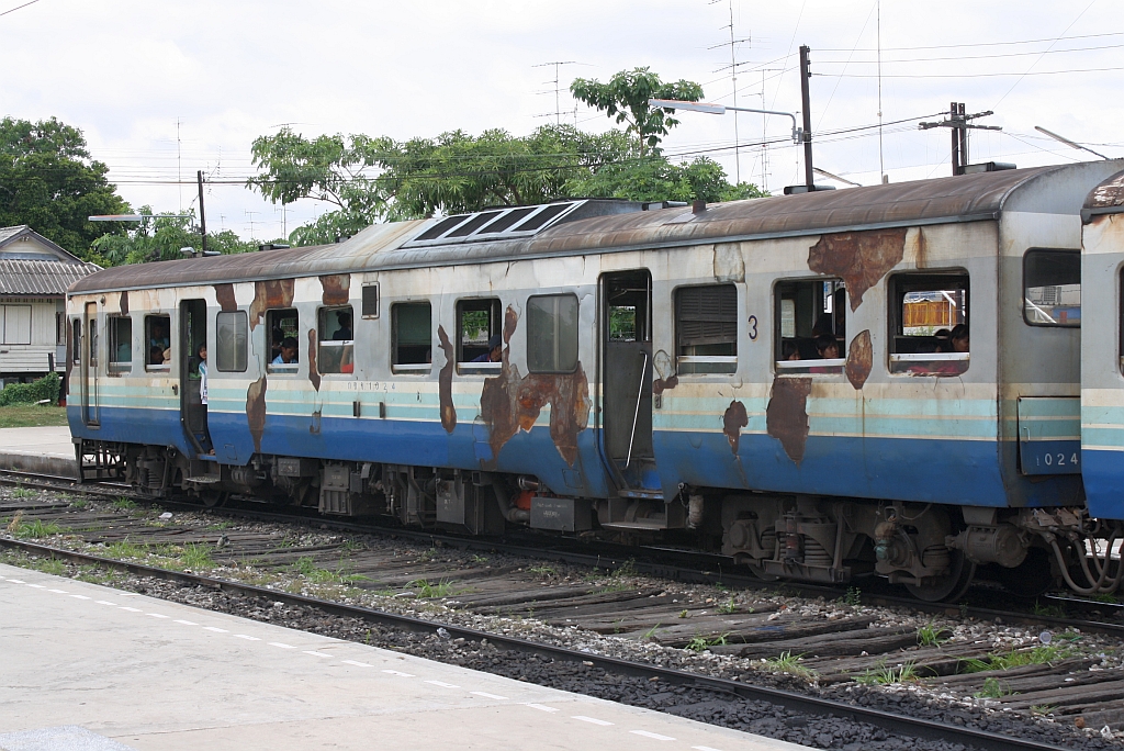 Hat wohl auch schon bessere Zeiten gesehen: กซข.1024 (กซข. = BPD/Bogie Power Diesel Railcar With Driving Cab, Hitachi/Nippon Sharyo, Bauj. 1971) am 18.Juni 2011 als ORD 434 nach Kaeng Khoi Jn. auf Gleis 1 des Bf. Bua Yai Junction.


