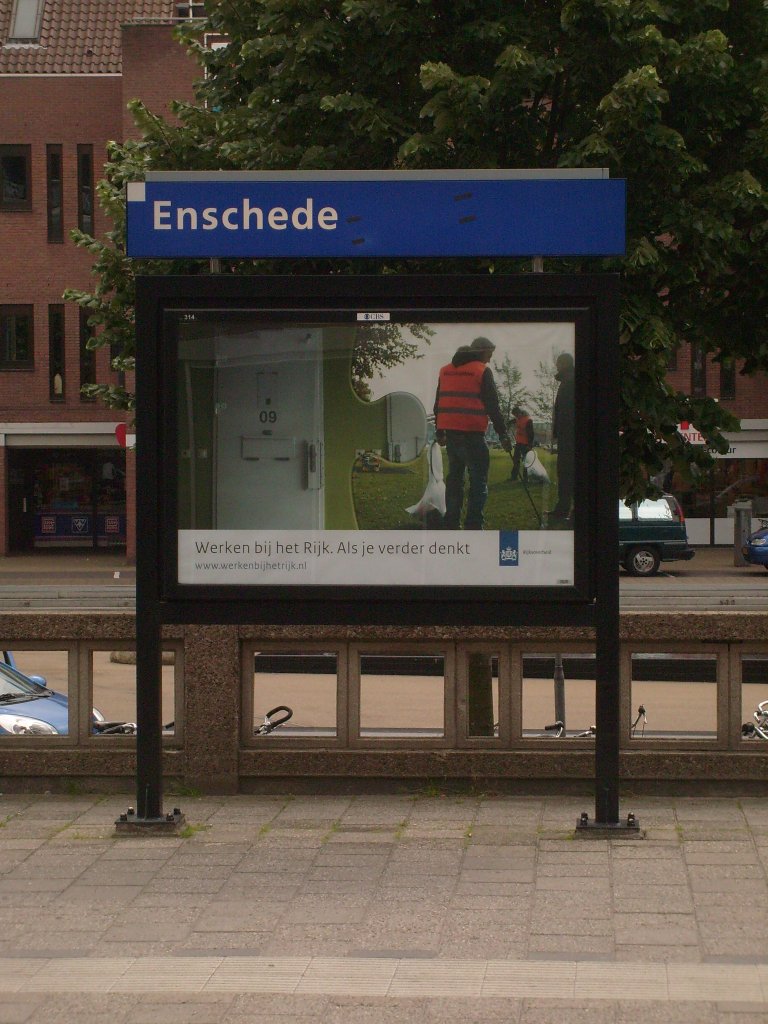 Hier noch zum Abschluss ein Bahnhofsschild inklusive Werbeplakat im Bahnhof von Enschede.