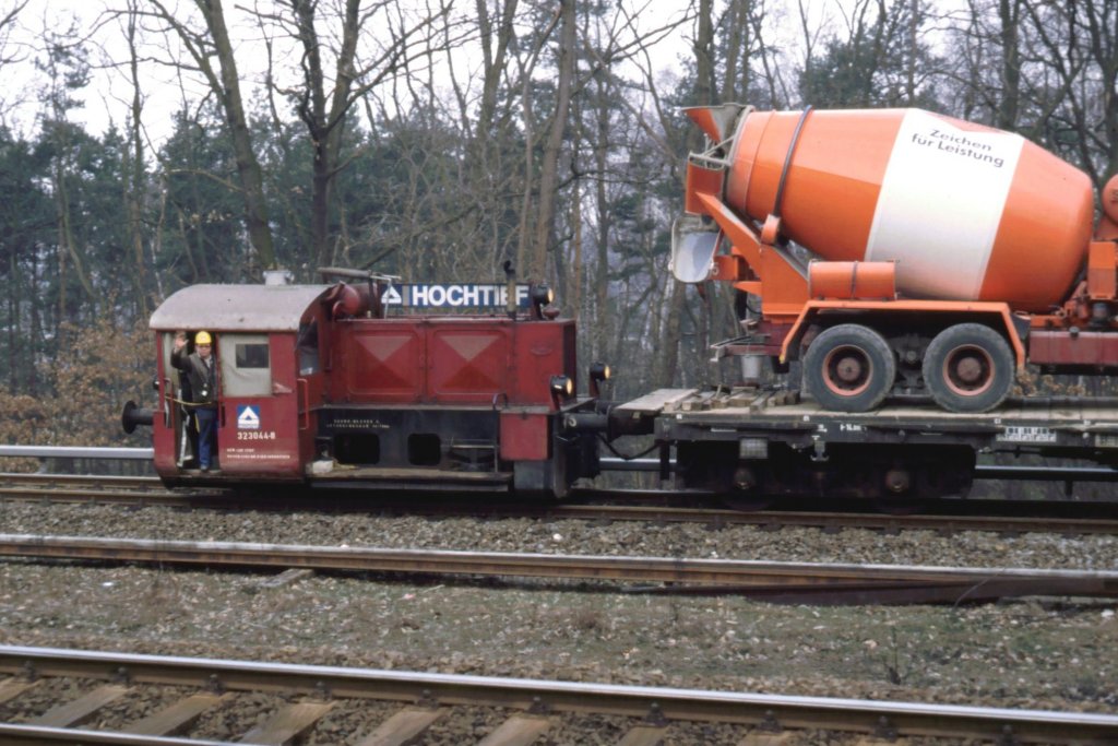Hoch & Tief Bauzuglok 323 044-8 in Berlin-Wannsee April 1987. Sie pendelt mit Flachwagen auf denen Betonmischer stehen.