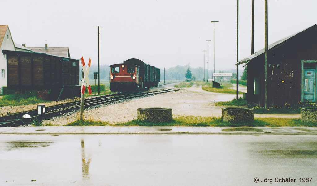 Im strmenden Regen fuhr der bergabezug im Mai 1987 durch den Haltepunkt Mhlhausen nach Neumarkt zurck. Bemerkenswert sind sowohl der ehemalige Gterwagen als Gterschuppen links wie auch das hlzerne Bahnhofsgebude rechts.