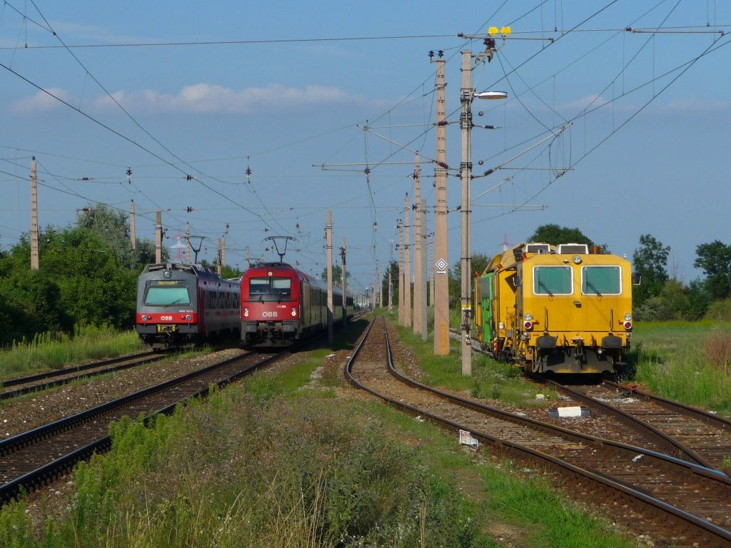 In Wien Sssenbrunn trifft eine Schnellbahngarnitur, bestehend aus einem roten Triebwagen (4020 320-0) und einem blauen Triebwagen 4020 262-4), auf die 1216.238. Abgestellt ist die Gleisschotterstopfmaschine X962 063-4.