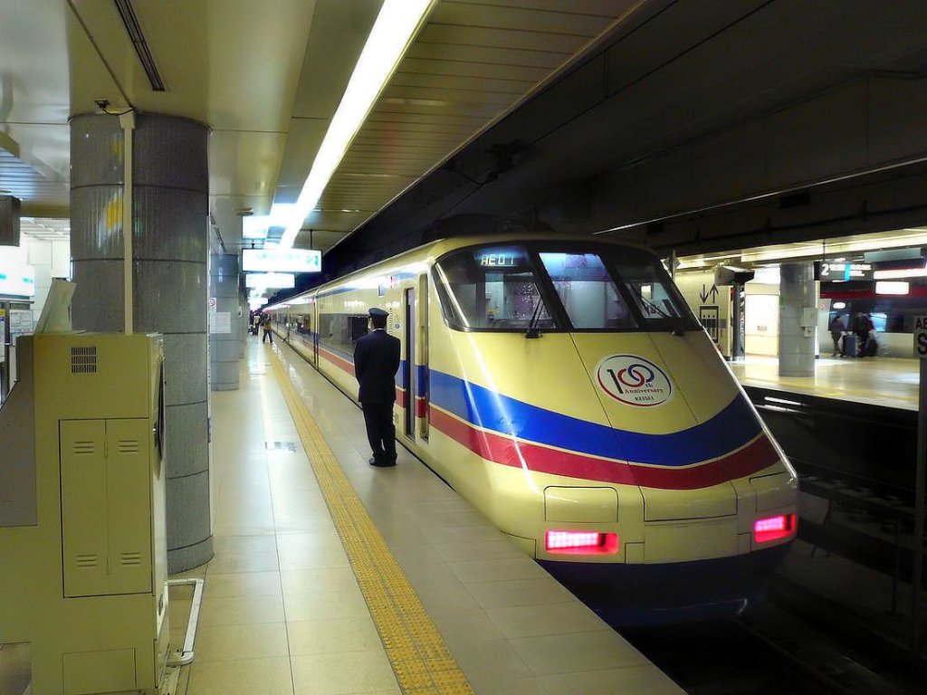 Keisei-Konzern, AE (Airport Express) Serie 100: Zug Nr.3 mit Endwagen AE 121 wartet in der Endstation Internationaler Flughafen Tokyo-Narita. Der Schaffner überwacht die Türen, ganz rechts aussen erkennt man einen Zug der JR (1067mm-Spur), der auf einer eigenen Strecke den Flughafen erreicht (der Keisei-Konzern hat 1435mm-Spur). 22.November 2009. 