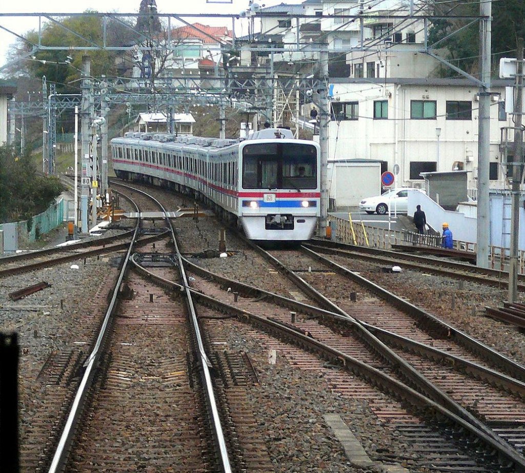 Keisei-Konzern, Serie 3400: 5 8-Wagenzüge dieser Bauart von Stahlwagen in grauem Anstrich entstanden 1991-1993 aus der Weiterverwendung von Untergestell und vielen Teilen der ersten Generation von Flughafenexpresszügen (Einsatz 1973-1993). Hier kommt der dritte Zug, Nr. 3421 (Endwagen 3428), in Keisei Sakura entgegen, 4.März 2010. (Aufnahme durch verglaste Führerstandrückwand eines Gegenzugs)