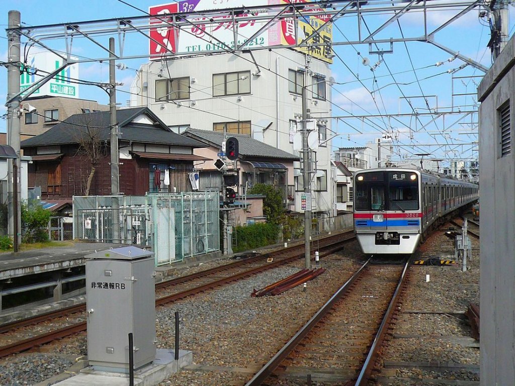 Keisei-Konzern, Serie 3700: Einer der beiden Sechswagenzüge, 3821 (mit Frontwagen 3828) fährt in Narita Stadt ein; er kommt aus dem Bereich des Service-Centers des Narita Flughafens. Links steht noch ein typisches Holzhaus aus den 1950/60er Jahren. 29.November 2009. 