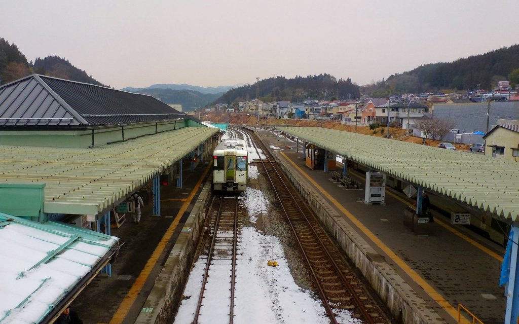 Kesennuma-Linie: Blick auf den etwas höher gelegenen Bahnhof Kesennuma - früher herrschte hier reger Betrieb, mit Zügen der Kesennuma-Linie von Süden her, Zügen der Ôfunato-Linie der Küste entlang nach Norden, und Zügen derselben Ôfunato-Linie hinauf durch die Berge ins Inland und zur Shinkansen-Verbindung in der Stadt Ichinoseki. Heute nach der Katastrophe verbleibt nur ein einsamer Triebwagen nach Ichinoseki (im Bild, Wagen KIHA 100-45, 15.Februar 2013). Die Bevölkerung von Kesennuma betrug 1980 noch über 90000, heute sind es weniger als 70000. 