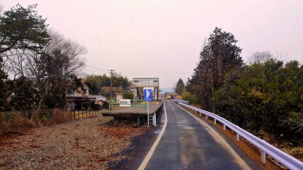 Kesennuma-Linie: Heute nach der Zerstörung der Strecke ist man dabei, einzelne Streckenteile als Bus-Spur herzurichten. Im Bild ist noch deutlich der Bahnhof Rikuzen Hashikami zu erkennen mit seinem Bahnsteig und der Ueberquerungsbrücke über die Geleise. Bei leichtem Schneefall, 15.Februar 2013. 