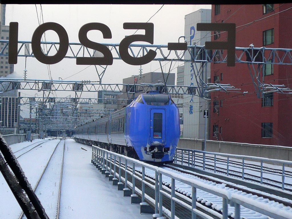 KIHA 281 (キハ281): Die Vorgänger der KIHA 283. Diese Neigezüge  Furico 281  wurden 1992-1994 gebaut, um die Fahrzeit zwischen Hakodate (dem heutigen Endpunkt der elektrischen Seikan-Tunnellinie von der japanischen Hauptinsel Honshû her) und Sapporo (der Hauptstadt von Hokkaidô) auf 3 Stunden zu drücken. Die Fensterpartie und die Stirnlampenanordnung sind deutlich anders als bei den KIHA 283. Es gibt 8 Kopfwagen KIHA 281, 15 Zwischenwagen KIHA 280, und 4 Wagen mit Luxussitzplätzen KIRO 280. Im Bild KIHA 281-901 in Sapporo, 16.Februar 2009. (Aufnahme durch die verglaste Führerstandrückwand eines Gegenzugs)  HAKODATE/MURORAN/CHITOSE-LINIE