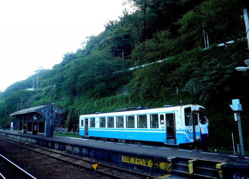 KIHA 32: Unterwegs in KIHA 32 5 (キハ32 5) - Der Wagen hat Iyo Nagahama ganz im Nordwesten der Insel Shikoku erreicht; während er auf den Gegenzug wartet, streckt sich der Wagenführer an der frischen Luft... 19.September 2009. 