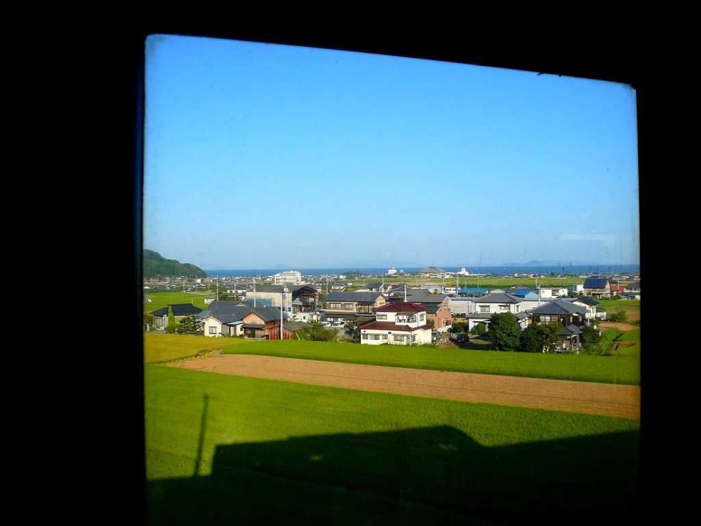 KIHA 32: Unterwegs in KIHA 32 5 - der Schatten fährt mit! An der Nordwestküste von Shikoku mit Blick auf die Inlandsee mit ihren unzähligen Inseln. Mukaibara, 19.September 2009. 