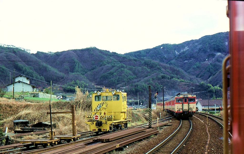 KIHA 58: Ausfahrt eines Zuges von KIHA 58-Triebwagen, vorbei an einem typischen Baudienstzug der damaligen Zeit. Bitchû Kawamo im Westen der japanischen Hauptinsel, 3.Januar 1978. 
