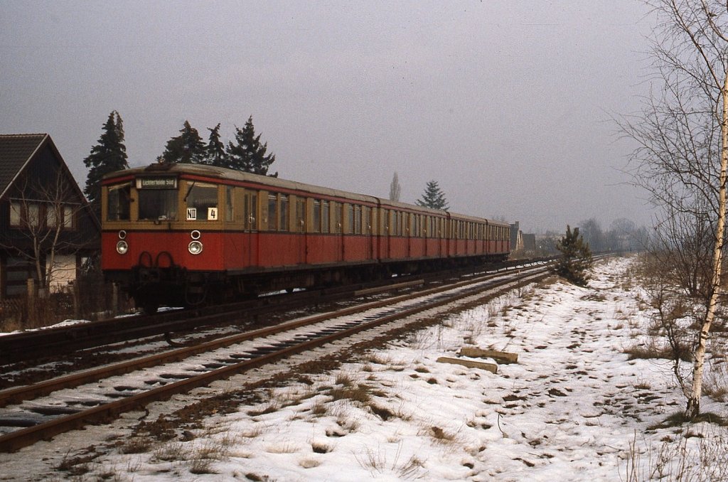 Kurz vor Lichterfelde Süd wurde dieser 275-Halbzug im Januar 1981 angetroffen. Ein Hinweis zur Beschilderung: Von 1980 bis 1984 verkehrten die Züge von Heiligensee nach Lichterfelde Süd als Zuggruppe N II. Anfang der 1950er Jahre wurden zur besseren Unterscheidung der Fahrtziele auf von mehreren Linien befahrenen Streckenabschnitten farbige Zielschilder eingeführt. Die weiße Schrift auf grünem Grund weist darauf hin, dass der Zug die Strecke Schönholz - Lichterfelde Süd befährt. Dieses System wurde etwa ab Mitte der 1970er Jahre aufgegeben, anscheinend wurde der aufgenommene Triebzug  vergessen .