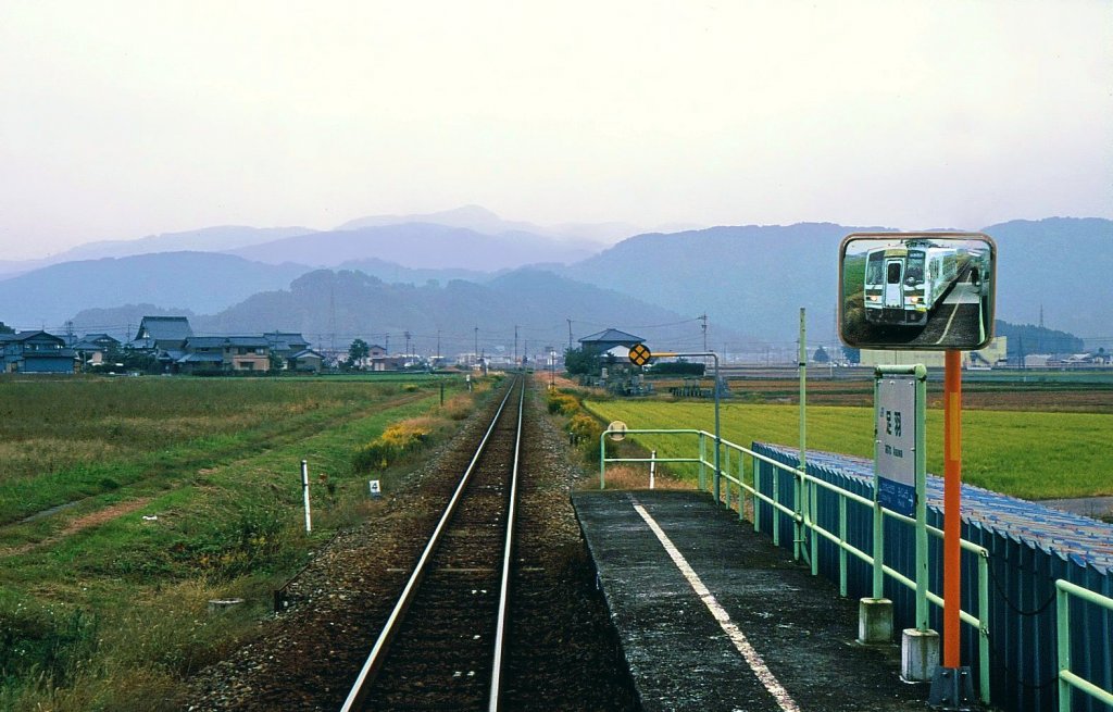 Kuzuryû-Linie: Wie in einem klassischen ostasiatischen Tusche-Gemälde verschwindet Hügelzug um Hügelzug im Dunst der Ferne. Dahin will Wagen KIHA 120-202 fahren, hier im Spiegel an der Haltestelle Asuwa, 3.November 2008. Im Dörfchen ragt das Dach des Ortstempels elegant in die Höhe. 