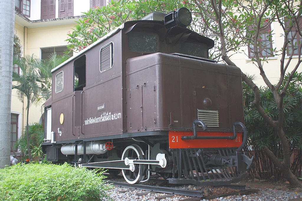 Links vom Haupteingang zum SRT-Head Quarter steht mit der  21  die erste Diesellok Thailands. Diese Lok wurde mit ihrer Schwester  22  von SLM 1928 gebaut, war 23,5t schwer, hatte einen 6 Zyl.-Reihenmotor mit 200PS bei 500U/min, Antrieb mittels Blindwelle und Stangen auf beide Achsen, und war 40Km/h schnell; Bild vom 16.Mrz 2011.