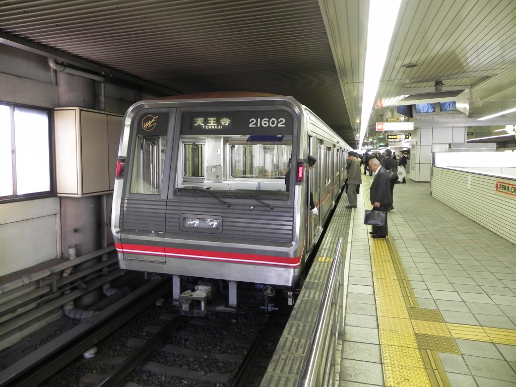 Midōsuji Line Series 21 Zug in der Haltestelle Shin-Osaka, von wo aus er in Richtung Tennoji abfahren wird. Der Zugbegleiter kontrolliert mit der  Zeige-und-Besttige -Methode den korrekten Halt des Zuges und wird gleich die Abfahrt kontrollieren und einleiten.