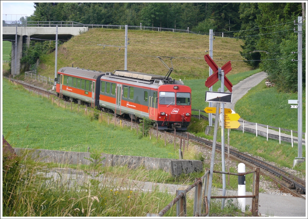 Nach dem berqueren der Kantonsstrasse bei der Haltestelle Kreuzstrasse beginnt ein neuer Zahnstangenabschnitt bis hinauf zum Stoss.R3094 mit BDeh4/4 16 und ABt 116 klettert bergwrts. Der Bahnbergang ber die viel befahrene Strasse wird ohne Schranke und Lichtsignal gequert, Schritttempo, ein Achtungspfiff und die rote Farbe des Zuges gengen offenbar. (28.07.2010)
