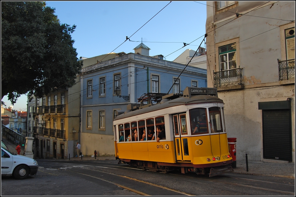 Neues Altes vom alten Ende der Welt (XX). Hier taucht die Eléctrico ab in die alte Welt der Alfama. Noch können sich die Fahrgäste nicht entscheiden, ob sie dem abenteuerlichen Verlauf der Straßenbahn, oder die Kirche Sao Vicente de Fora anschauen sollen, die das warme Abendlicht auf die Straßenbahn reflektiert. (Sommer 2010)