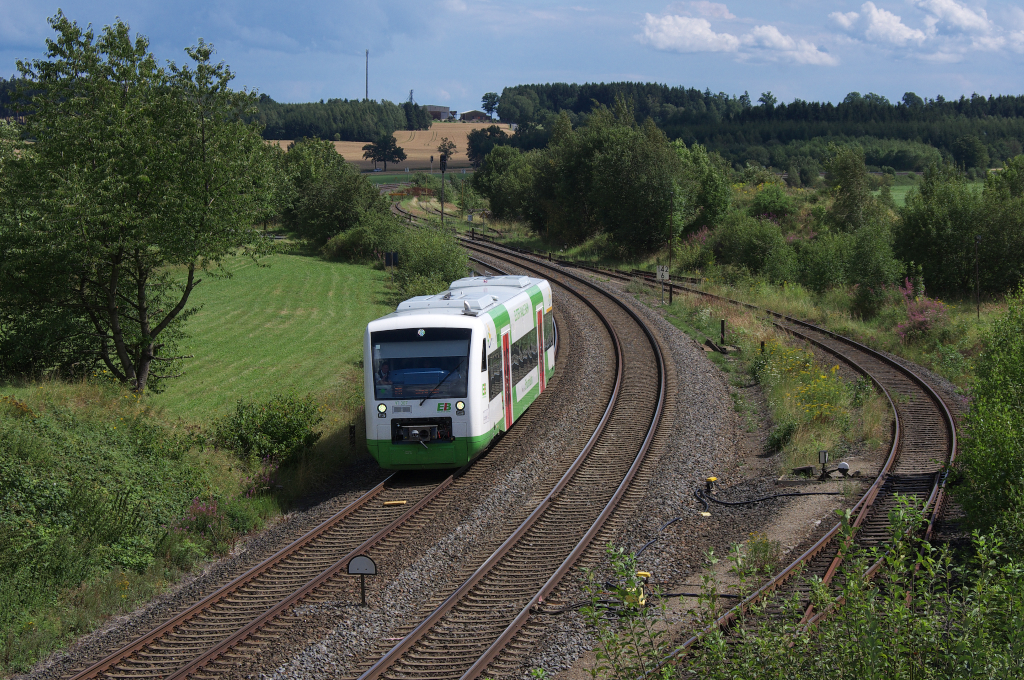 Regio Shuttle VT 307 ist auf dem Weg von Hof nach Gera. Nach Einstellung der RE Linie Regensburg - Gera bernahm ab Sommerfahrplan 2012 die Erfurter Bahn die Relation Hof - Gera. Die Fahrzeuge tragen die Beschriftung  Elster - Saale Bahn . Der Name ist bedingt durch den Fahrweg von Gera (Weie Elster) nach Hof (Saale). Der Name passt auch fr die ebenfalls von der EB bediente Relation Gera - Saalfeld.
Hier ist der Triebwagen bei Reuth/Vogtland unterwegs. In Mehltheuer wird er von der Strecke Hof - Plauen oberer Bahnhof - Werdau - Leipzig abbiegen und ber Zeulenroda und Weida nach Gera fahren.
03.08.2012