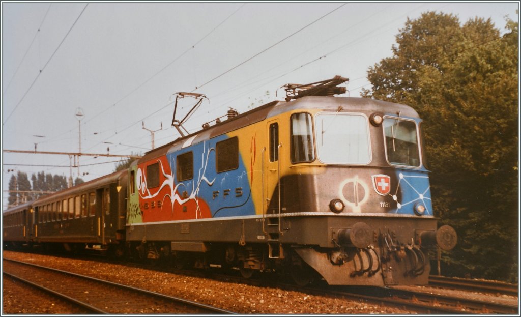 Seit dem 7. Juli 1983 verkehrte die Re 4/4 II 11181 in bunten Farben, aufgemalt vom Künstler Daniel Bourret. Mit der fälligen R3 im Jahre 1984 wurde die Lok rot lackiert.
Auf dem hier überarbeiteten Bild ist die Re 4/4 II 11181 mit dem Schnellzug 536 in Grenchen Süd zu sehen.
27. August 1984