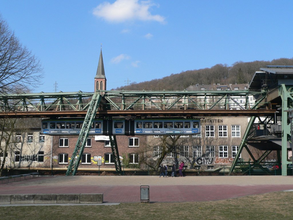 Seitenansicht einer Schwebebahn bei der Einfahrt in der Pestalozzistraße. Oben die Schwebebahn, unten die spielenden Kinder. Während der Bahnfan extra anreist, sind die Kinder völlig unbeeindruckt. 2.4.2013