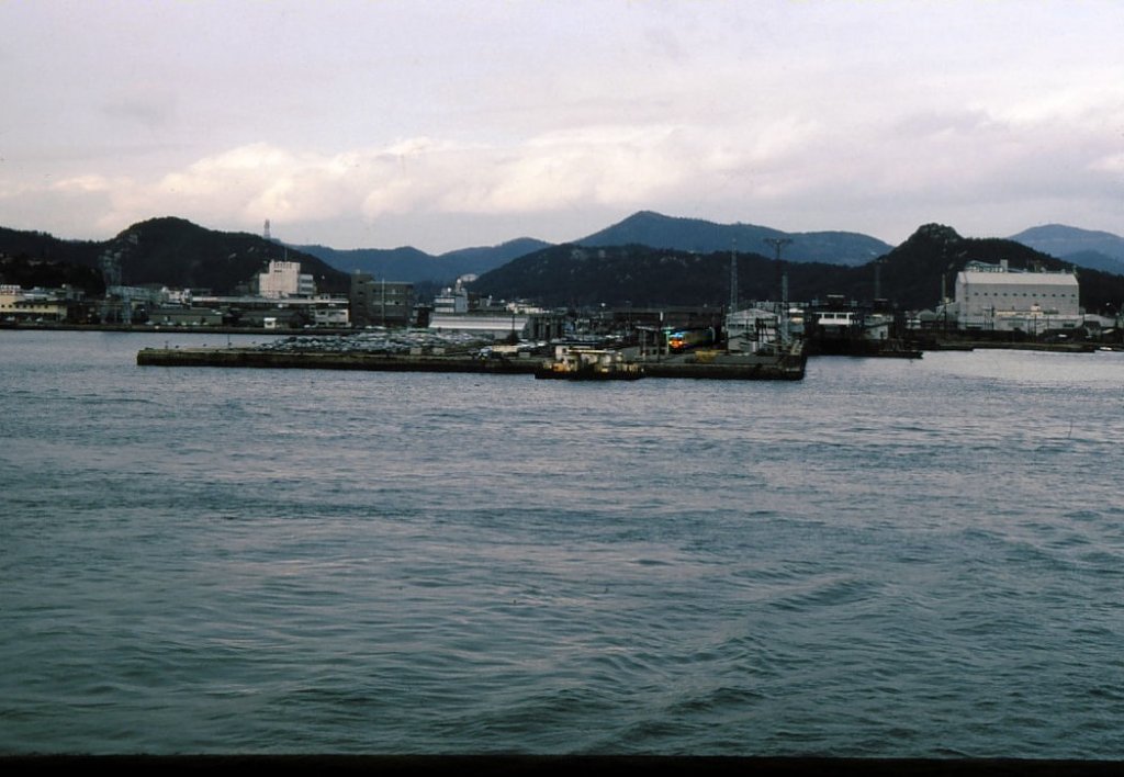 Serie 111 u.113 - auf der Verbindung zwischen Japans Hauptinsel und Shikoku: Von der ausfahrenden Shikoku-Fähre  Tosa-maru  erscheint der an der Endstation Uno verbliebene Zug mit Steuerwagen KUHA 111-335 ganz winzig klein. 30.Dezember 1978. 