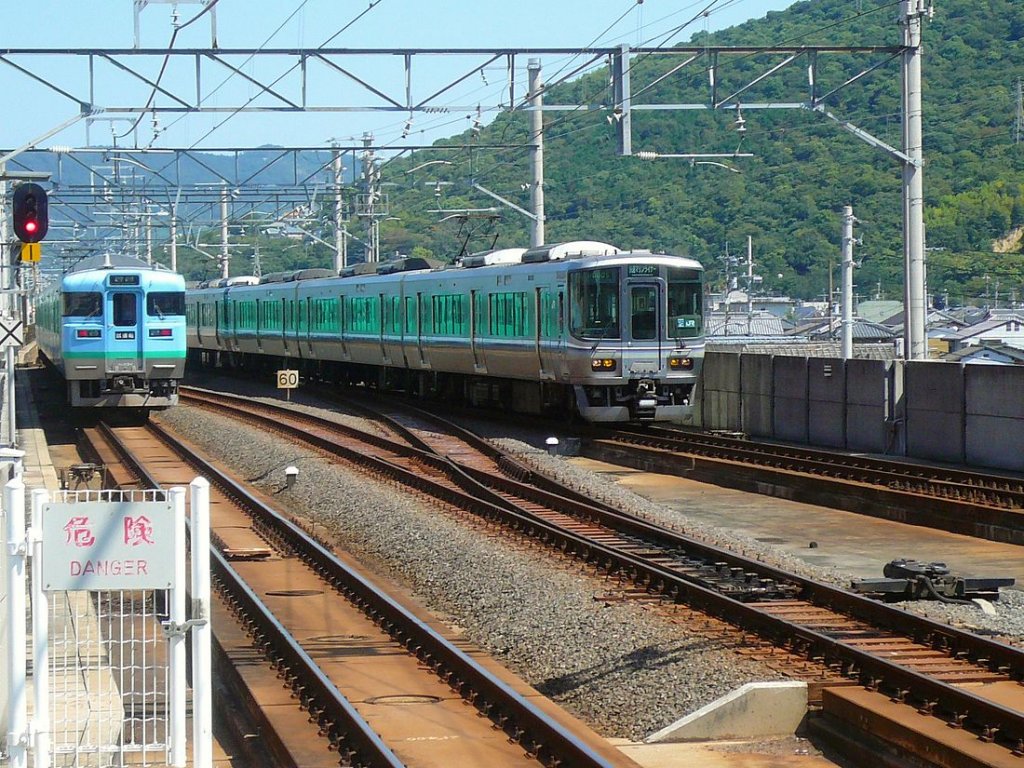 Serie 111 u.113 - auf der Verbindung zwischen Japans Hauptinsel und Shikoku: Zug Nr. 1 (sichtbar westseitiger Steuerwagen KUHA 113-1) der JR Shikoku (hellblau/grün) in Sakaide. Rechts kommt ein Zug der Serie 223 von JR Westjapan entgegen, der in wenigen Minuten über die Grosse Seto-Brücke auf die japanische Hauptinsel zurückkehren wird. 17.September 2009. 
