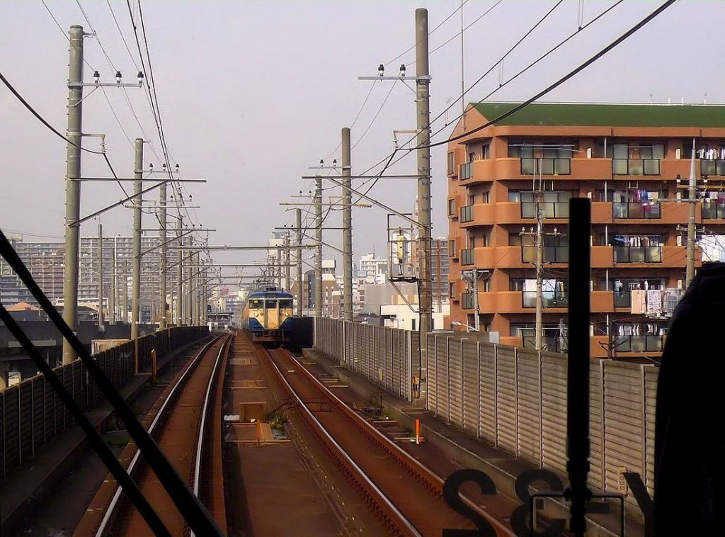 Serie 111/113 am Rande der Agglomeration Tokyo: In der Stadt Chiba (1 Million Einwohner) hat ein entgegenkommender Zug mit Steuerwagen KUHA 111-2154 gerade die Station Hon-Chiba verlassen. 27.November 2009. 