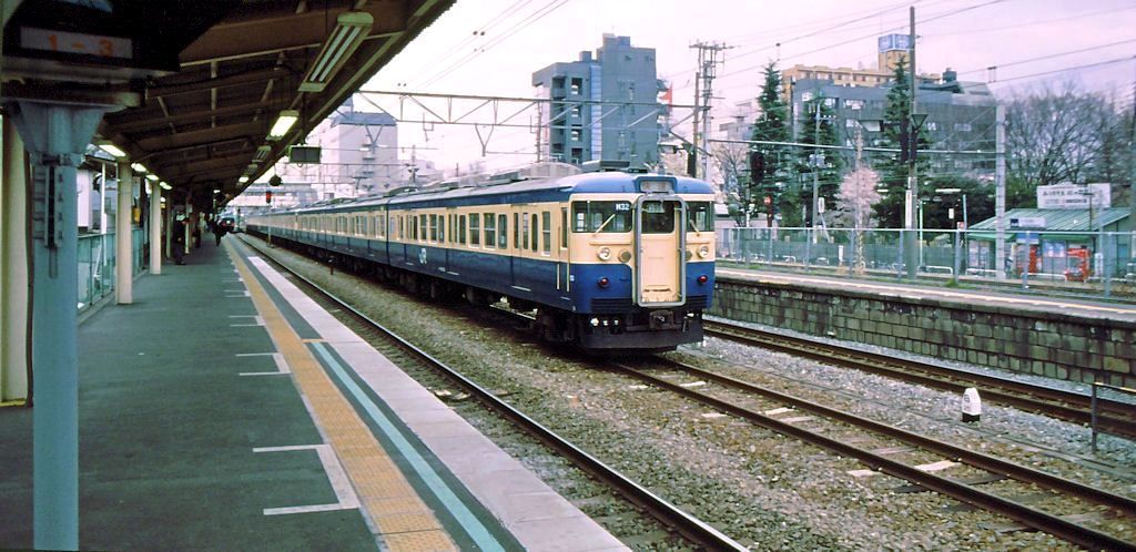 Serie 115 des zentraljapanischen Hochlands: In Tokyo-Musashi Sakai stehen mehrere 3-Wagenzüge auf einem Nebengleis. Es handelt sich um Wagen im traditionellen dunkelblau/weissen Anstrich, die in West-Tokyo beheimatet sind. Zuvorderst Steuerwagen KUHA 115-182. 4.April 1999. 