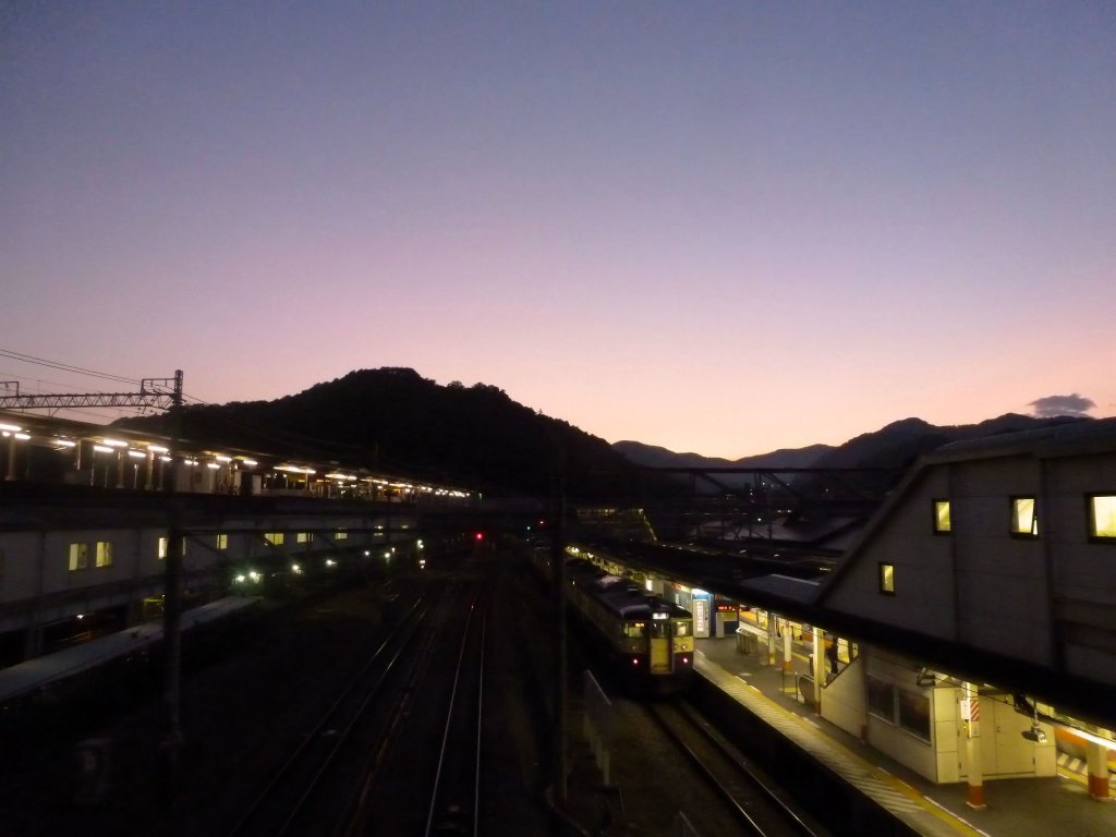 Serie 115 des zentraljapanischen Hochlands: Am Rande von Tokyo nach Sonnenuntergang beginnt der Zug mit Endwagen KUMOHA 115-305 seine Fahrt in die Berge hianuf. Takao, 23.Oktober 2011. 