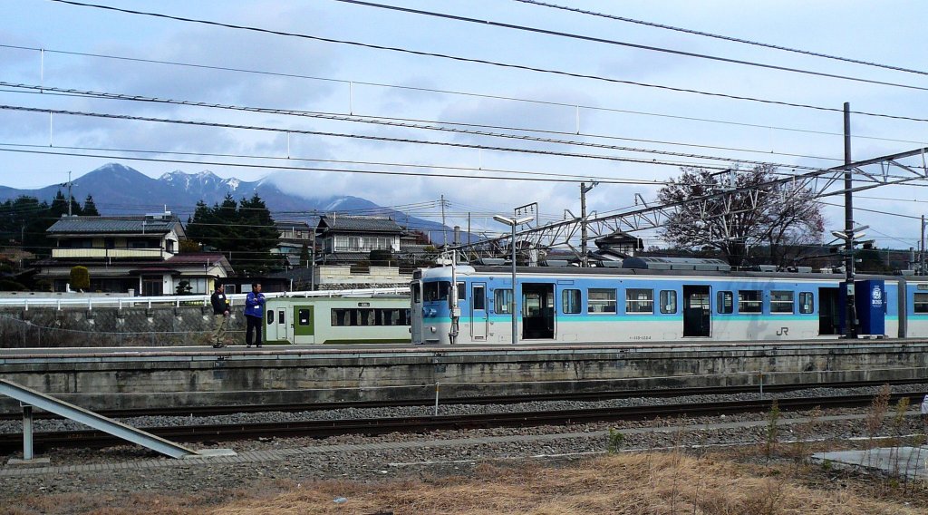 Serie 115 des zentraljapanischen Hochlands: Der Endwagen eines 6-Wagenzugs KUHA 115-1224 in Kobuchizawa; im Hintergrund ein Dieseltriebwagen der Koumi-Linie, Japans höchstgelegener Bahnlinie. 24.November 2009. 