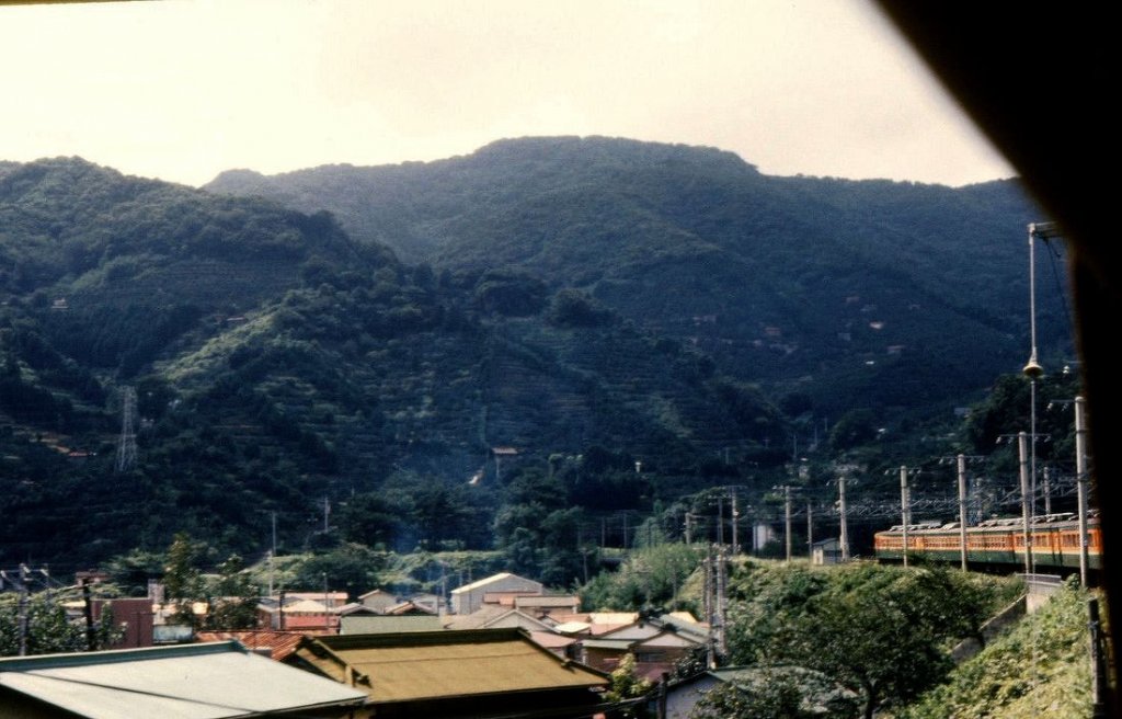 Serie 153: Früher waren die Schnellzüge noch nicht klimatisiert, so dass man bei offenem Fenster hinausschauen konnte. In einem Zug Serie 153 auf der alten Tôkaidô-Linie im Vulkangebiet westlich von Tokyo. Die 3. und 4. Wagen haben Luxussitzplätze und sind mit einem breiten grünen Streifen gekennzeichnet. Yugawara, 27.August 1977. 