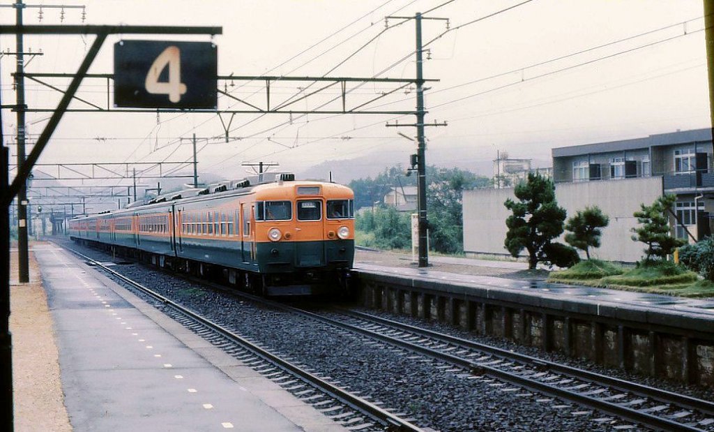 Serie 165: An einem nassen Tag fährt ein Schnellzug mit Steuerwagen KUHA 165-181 durch Shinjohara an der alten Tôkaidô-Linie, 27.August 1977.