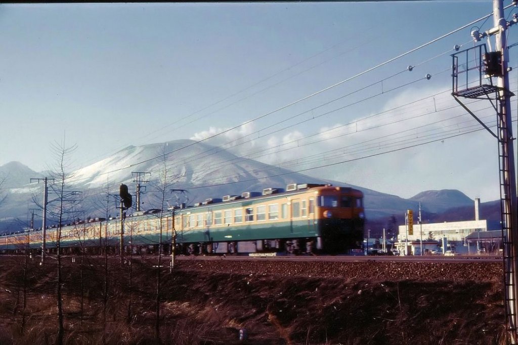 Serie 169: 1967-69 entstand für die Strecke nach Nagano mit der Usui-Rampe (11,2 km lang, 66,7 Promille Steigung) die Serie 169 für Schnellzüge, die von talseitigen Schiebe- und Bremslokomotiven (Serie EF63) ferngesteuert werden konnte. 31 Motorwagenpaare, 31 Steuerwagen, dazu 19 Luxuswagen (aus Serie 165 umgebaut) und 10 Speisewagen (aus Serie 153; bis 1979 ausgeschieden). Die Serie 169 ist bei der JR 2003 ausgeschieden, 12 Wagen sind noch bei der Shinano Bahn im Einsatz. Aufnahme bei Naka Karuizawa, rechts ein Motorwagenpaar mit Frontwagen KUMOHA 169-14, links davon 2 Luxuswagen und der Speisewagen. 13.Februar 1973. 