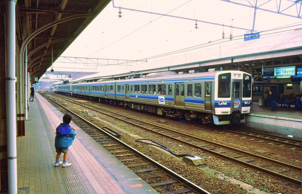 Serie 213: JR West beschaffte Dreiwagenzüge mit bequemem Innenraum für den Dienst über die 1988 eröffnete riesige Seto-Brücke von Okayama hinüber auf die Insel Shikoku. 6 Züge hatten Panorama-Steuerwagen (Serie KURO 212); einer ist am anderen Ende des Zugs im Bild zu erkennen. 2003 wurden diese Züge wegen Problemen mit Salzwasser, Rückgang der Passagierzahlen und Uebernahme der vorderen Zugseinheit durch JR Shikoku-Rollmaterial von der Linie über die grosse Seto-Brücke abgezogen. Im Bild 2 Dreiwagenzüge, vorn KUMOHA 213-6 (motorisiert, mit Führerstand)+SAHA 213-6 (unmotorisiert)+KUHA 212-6 (Steuerwagen), Okayama, 25.März 1991.