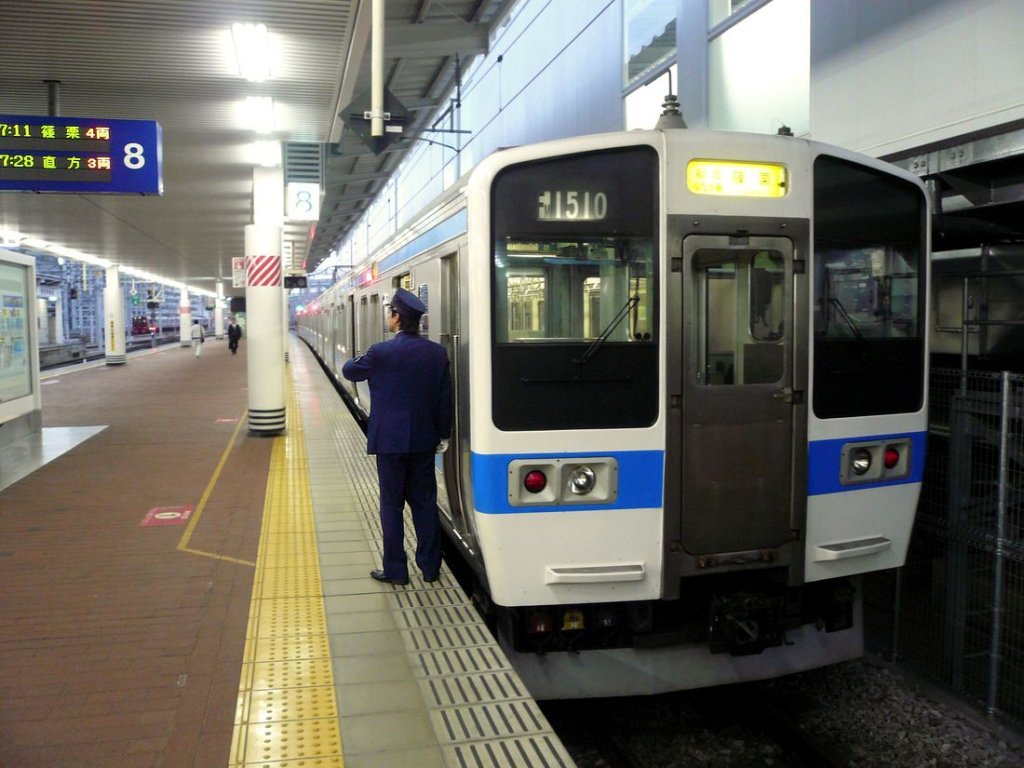 Serie 411/415: Ein neuerer Zug mit Wagen aus rostfreiem Stahl in Hakata (Stadt Fukuoka). Endwagen KUHA 411-1610. Der Schaffner zählt offenbar die Sekunden bis zur Abfahrt! 28.November 2010.