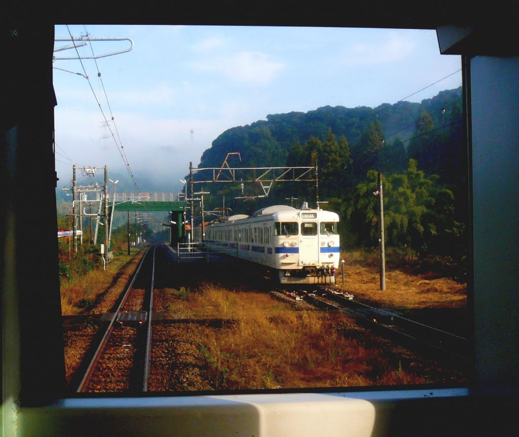 Serie 411/415: Zug mit Steuerwagen KUHA 411-515 fährt im Morgennebel aus der Haltestelle Koban Chaya im Südwesten der Südinsel Kyûshû aus. 1.Dezember 2010. (Photo durch die verglaste Führerstandrückwand eines Gegenzugs)