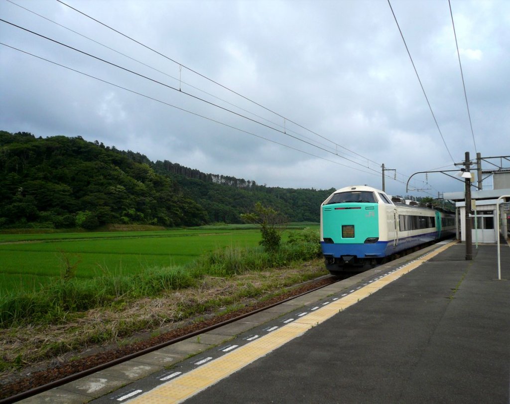 Serie 481 / 485-3000: Ein umfassend modernisierter Zug durchfährt die Station Ugo Kameda ganz im Nordwesten der japanischen Hauptinsel. Man erkennt das üppige Grün der besonders hochwertigen Reisfelder dieser Gegend. Endwagen mit gewöhnlichen und Luxus-Sitzplätzen KUROHA 481-3020, 10.Juli 2010. 