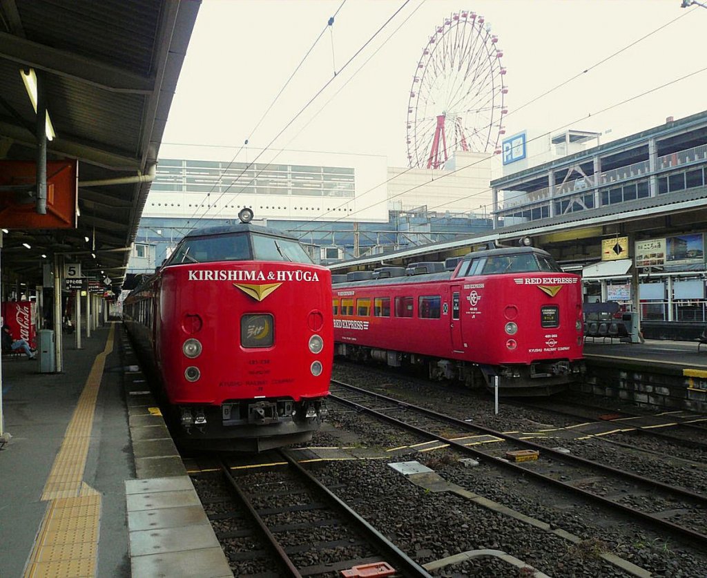 Serie 481 / 485: Die auf der japanischen Südinsel Kyûshû eingesetzten Züge sind im bevölkerungsreichen Norden durch neuere ersetzt und in den äussersten Süden abgedrängt worden. Im Zentralbahnhof der Stadt Kagoshima mit seinem markanten Riesenrad stehen links ein 3-Wagenzug für Pendler aus der Region, die zur Morgenstosszeit mit einem zuschlagspflichtigen Zug reisen wollen (Endwagen KUHA 481-238), rechts ein 5-Wagen-Intercityzug von Kagoshima über die Berge nach Miyazaki in Ost-Kyûshû (Endwagen KUROHA 481-203 mit gewöhnlichen und Luxussitzplätzen). Kagoshima Chûô, 1.Dezember 2010. NIPPÔ-HAUPTLINIE
