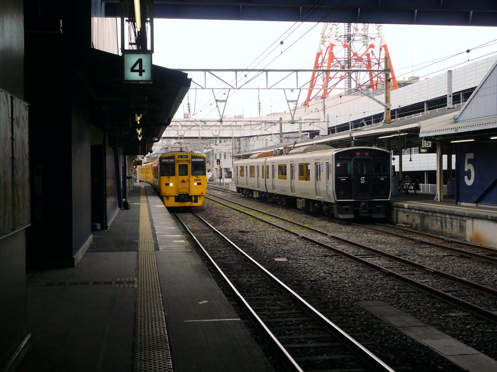 Serie 817: Während Zug Nr.8 auf Abfahrt in die Berge westlich von Kagoshima wartet, trifft ein Dieselzug von Japans südlichster Bahnlinie in Kagoshima Zentralbahnhof ein. 30.November 2010. 