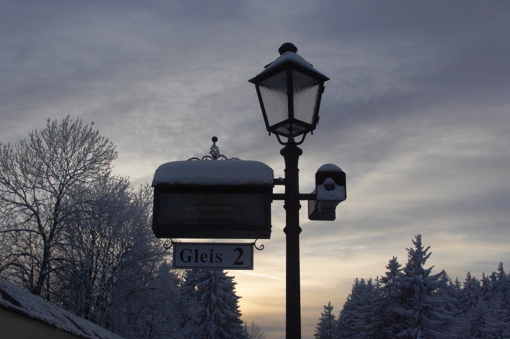 Silhouette einer Bahnsteiglaterne mit Zugzielanzeiger vor winterlichem Abend-Gegenlicht, aufgenommen am 26.01.2013 im Bahnhof Drei Annen Hohne.
