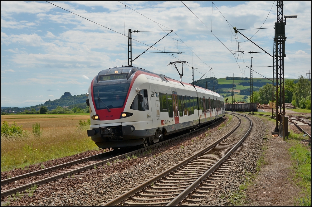 Sommertag im Hegau. Der Seehas 521 206 erreicht soeben den Bahnsteigbereich von Welschingen. Links im Hintergrund, durch das Weitwinkel noch kleiner der Hohenkrhen. Zwar der kleinste Hegauvulkan, dafr aber mit eigenem Burggespenst, dem Poppele. Juli 2012.